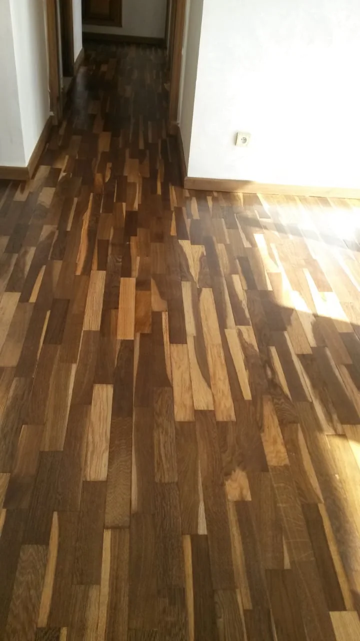 Raccord de parquet brun entre un couloir et une pièce blanche