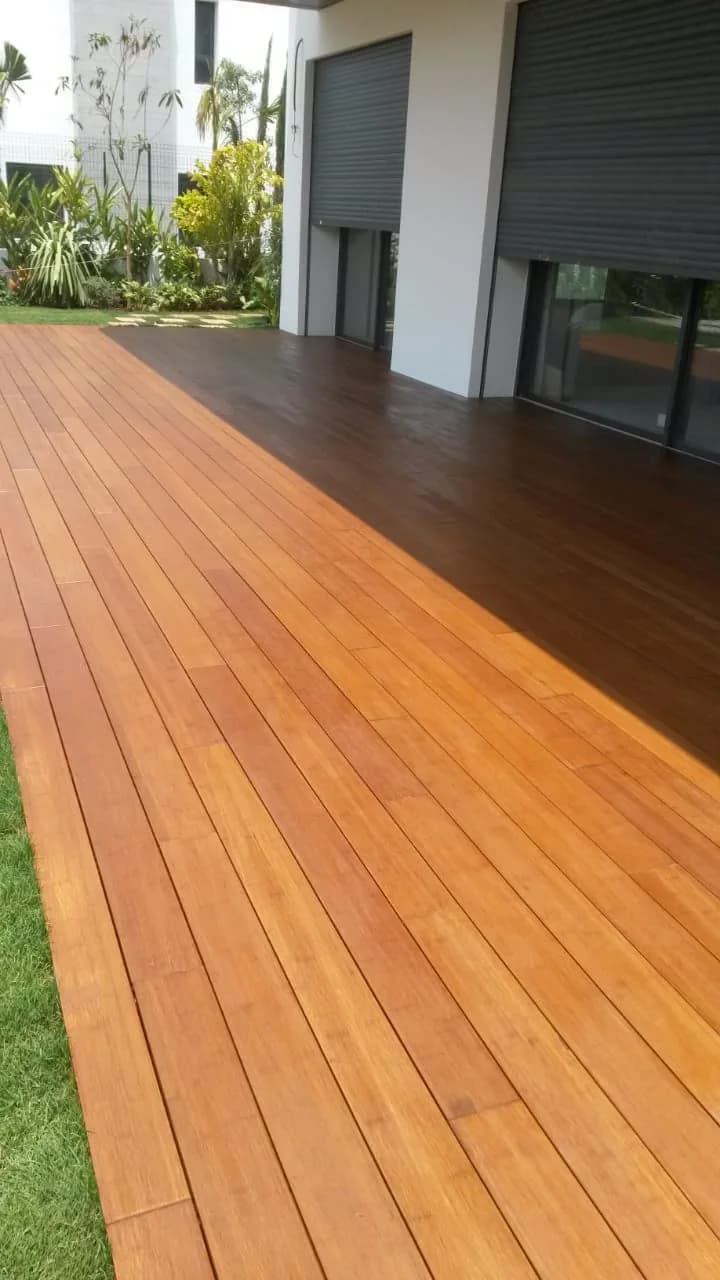 Lames de terrasse en bois longeant une baie vitrée et un jardin